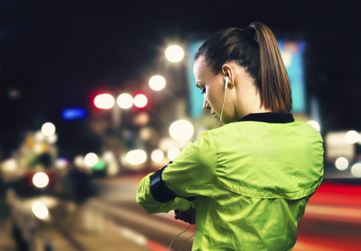 Woman in green jogging at night with headphones